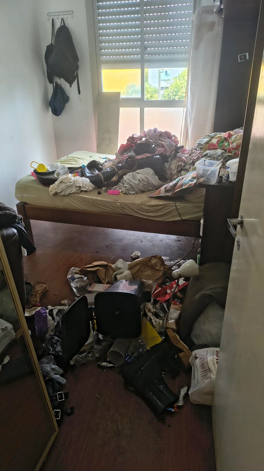 Bedroom floor covered in clothes, bags, and trash before junk removal in Queens