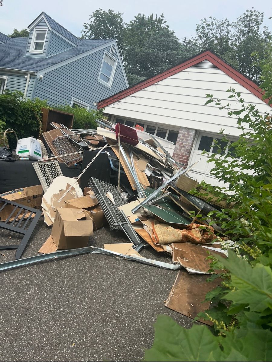 Driveway piled with furniture, shelving, and debris before junk removal in New Hyde Park